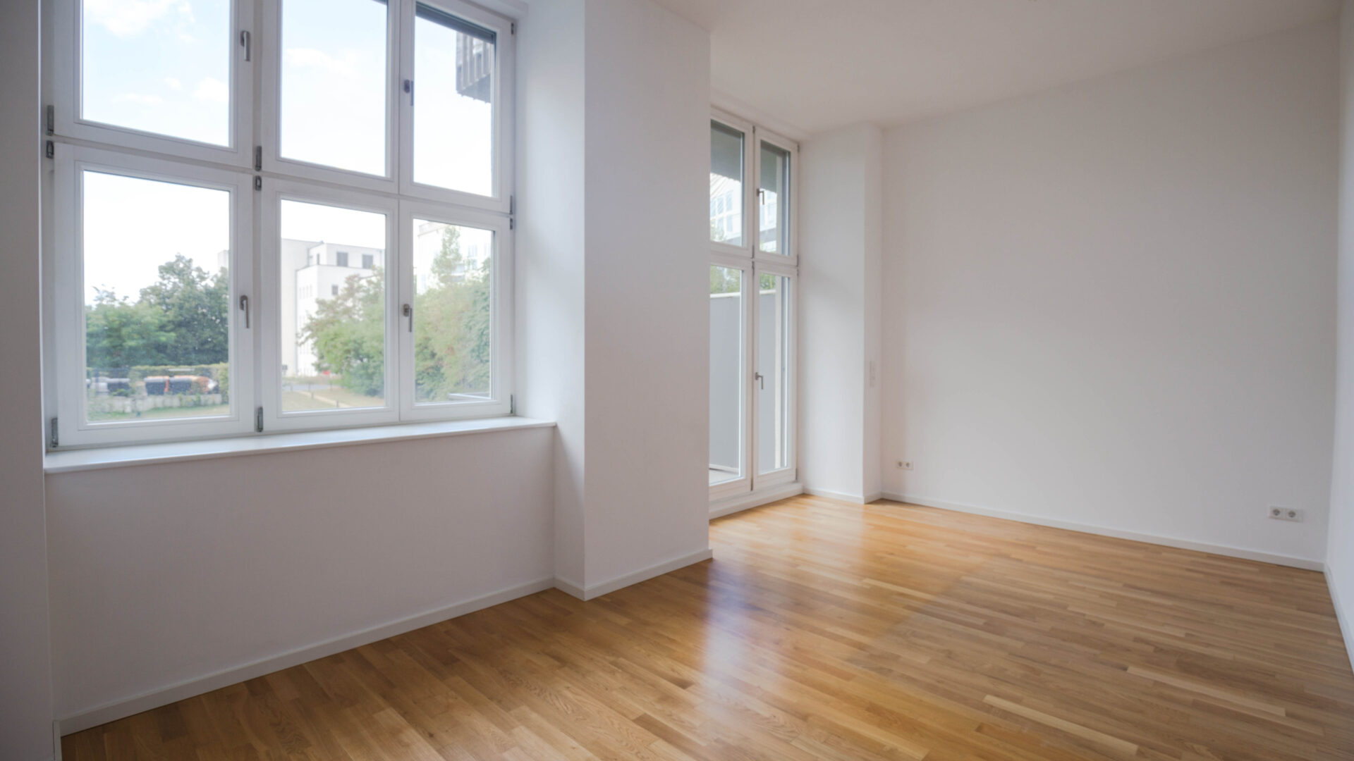 Innenraum einer modernen unmöblierten Wohnung im 1. Obergeschoss mit großen Fenstern und Balkonausgang in Berlin-Lichterfelde.