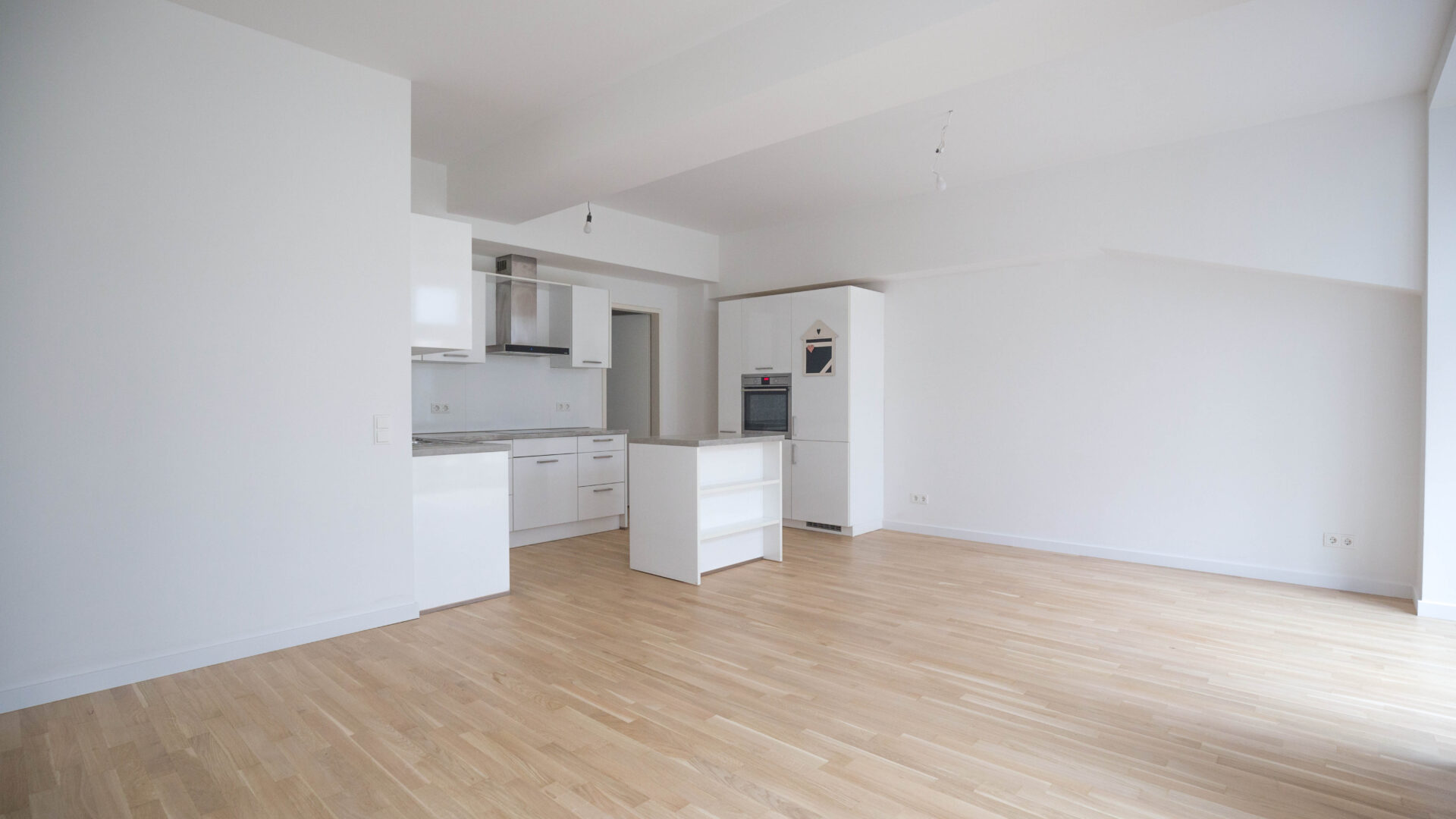 Innenansicht auf eine moderne weiße Einbauküche mit Küchenblock in einem modernen Wohn-Ess-Zimmer.
