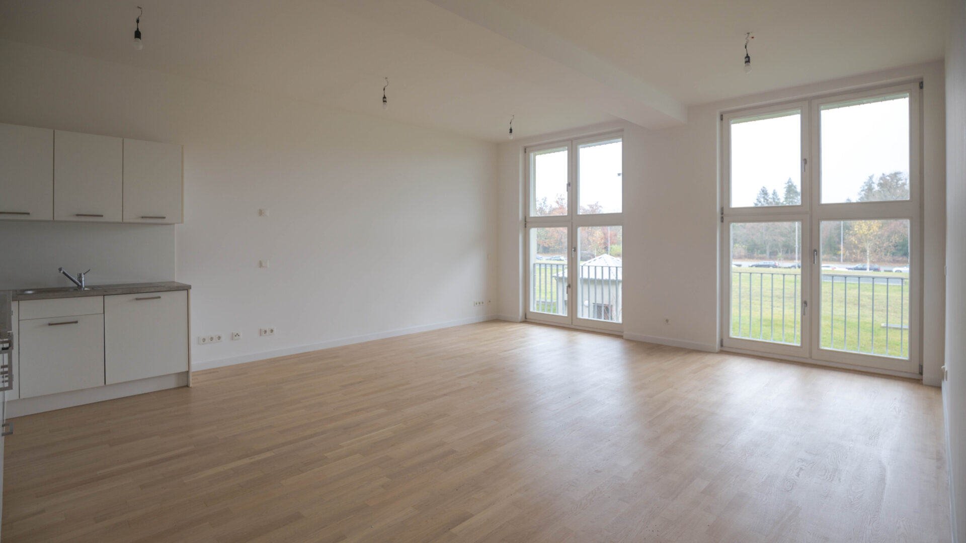 Innenraum einer modernen unmöblierten Erdgeschoßwohnung mit zwei großen bodentiefen Fenstern und Blick auf eine Terrasse in Berlin-Lichterfelde