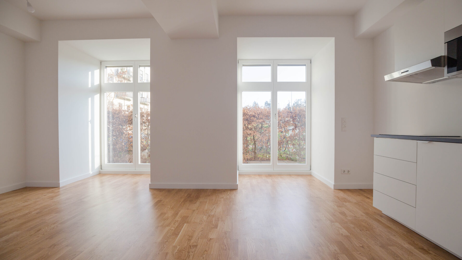 Innenraum einer modernen unmöblierten Erdgeschoßwohnung mit zwei großen bodentiefen Fenstern und Blick auf eine Terrasse in Berlin-Lichterfelde