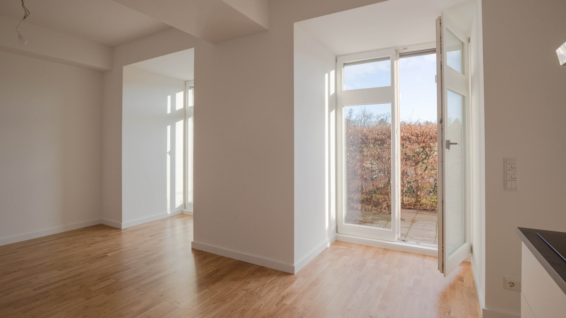 Innenraum einer modernen unmöblierten Erdgeschoßwohnung mit zwei großen bodentiefen Fenstern und Blick auf eine Terrasse in Berlin-Lichterfelde